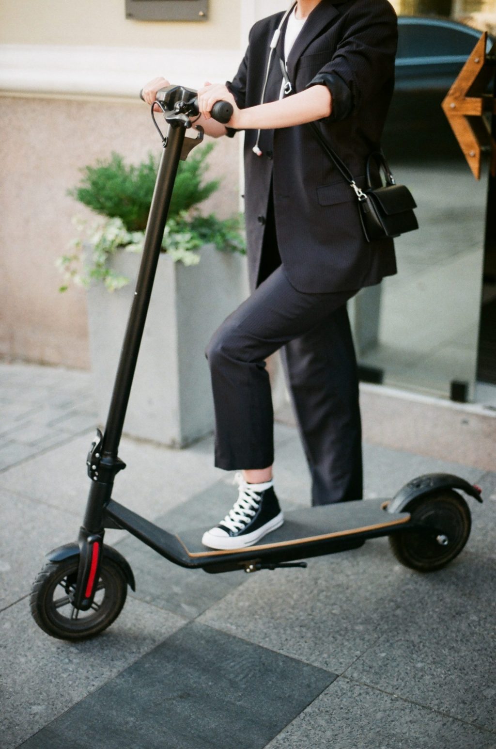 woman wearing office suit and converse stepping on scooter